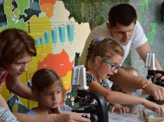 2 dzieci wraz z opiekunami podczas warsztatów edukacyjnych z mikroskopami.